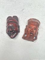 Photo showing front view of both carved masks side by side on a white surface.