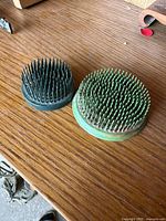 Two circular flower frogs with multiple metal spikes packed tightly, placed on a wooden surface.