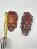 Pair of Chinese carved wooden masks, showing size with tape measure and both masks side by side.