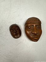Two wooden carved masks side by side on a white surface showing size difference and details.