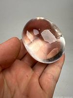Clear polished quartz orb held in hand showing smooth surface and internal inclusions.