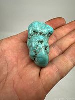 Raw turquoise stone held in hand showing size and color