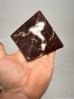 Photo showing red marble pyramid held in hand, highlighting size and white natural veining on the reddish surface.