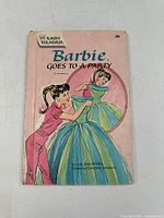 Front cover of 'Barbie Goes To A Party' Easy Reader book, showing Barbie in pink dress helping with a blue and green dress, with wear and creases on cover.