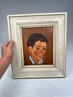 Framed vintage painting on wood board portraying cartoon-style boy portrait. Shows overall view of painting and frame.