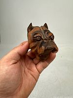 Front view of hand carved wooden bulldog head held in hand showing detailed facial features and wood texture