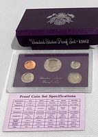 Front of proof set with five obverse coin faces, lens, slip-case and spec card