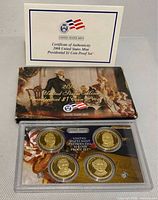 Front view of plastic-encased four-coin proof set with outer sleeve and certificate