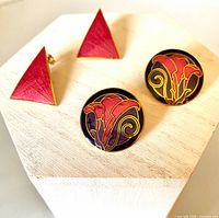 Front view showing both pairs: triangular red enamel studs and round black floral enamel studs