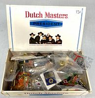 Open Dutch Masters box showing assorted lapel pins in plastic bags