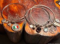 Overview of two of the three silvertone charm bangles showing Italian flag charm and assorted other charms