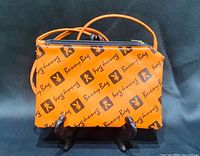 Front view showing orange bag, logo pattern, zipper, strap