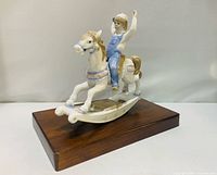 Front angled view of porcelain boy on rocking horse figurine on wooden base