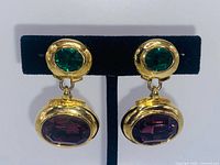 Front view of both clip-on earrings on display stand showing green top stones and purple dangles