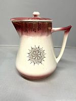 Front view of cream and rose ceramic pitcher with starburst crest and lid