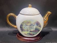 Full view of teapot with lid showing gold handle/spout and printed scene