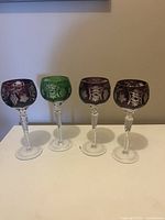 Front view of the four colored wine glasses arranged side by side, showing their etched patterns and colors