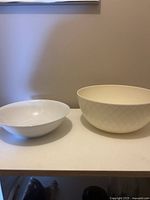 Two ceramic bowls, one medium white and one large cream with subtle diamond texture, displayed on shelf.