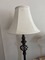 Front view of the black metal floor lamp showing the white fabric bell-shaped shade and decorative twisted metalwork on the stem.