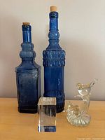 Front view of two blue glass bottles with cork stoppers, New York glass paperweight, and clear glass bird ornament