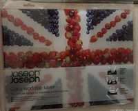 Front view of the glass cutting board in original packaging, showing the Union Jack pattern made of fruits and Joseph Joseph branding.