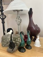 Full collection of 8 animal figurines and bookends displayed on a wooden surface including green glass swans, large brown wooden duck, white and red birds, black bear on rock, black and white bird on rock.
