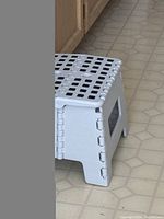 Gray plastic folding step stool, folded up showing side profile with hinge details and vented design