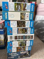 Stack of 8 jigsaw puzzle boxes showing various brands and piece counts