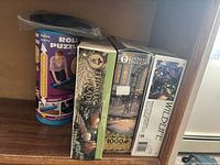 Shelf photo showing the three puzzle boxes and the Buffalo Games puzzle mat beside them.