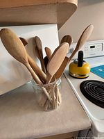 View of mixed wooden spoons in clear glass jar on kitchen counter near stovetop