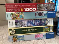 Stack of 5 jigsaw puzzle boxes showing brands, piece count, and titles.