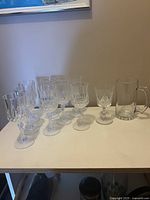 Set of 9 crystal wine glasses with faceted design and 1 clear glass beer mug on table