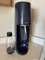 Dark blue SodaStream soda maker with included clear plastic bottle with black screw cap shown on kitchen counter.