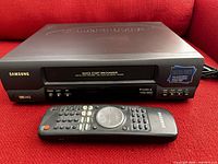 Samsung VHS player with remote control shown on a red surface.