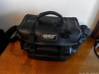 Black Optex branded carrying case with buckle closures and handle, placed on wooden surface.