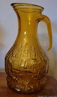 Front left angle view of amber glass water pitcher showing texture details and curved handle.