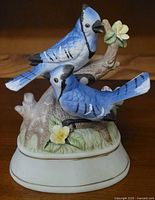 Front view of ceramic musical figurine featuring two blue jays on a branch with flowers, showing detailed painting and oval base