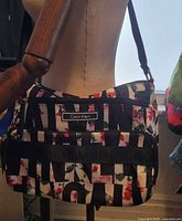 Photo of a Calvin Klein purse displayed on a mannequin showing the front and side views of the purse with visible floral and lettered pattern and metal logo plate.