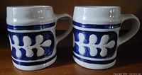 Photo showing two Colonial Williamsburg pottery mugs with cobalt blue and white leaf design from front angle.