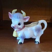 Front-side view of the cow creamer showing face, horns, bell, and tail handle.