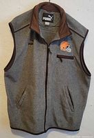 Full front view of the grey fleece vest showing the zipper, two side pockets, brown collar lining, and Cleveland Browns helmet logo on the left chest.