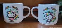 Two white ceramic mugs side by side with Hello Kitty dressed as a unicorn and colorful 'Hello Kitty' text.