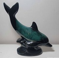 Front diagonal view of blue-green glazed dolphin figurine on black base