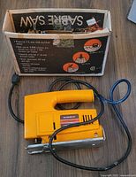 Yellow Mastercraft sabre saw with black cord placed next to its original box showing brand and features.