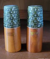 Front view of two mid-century modern salt and pepper shakers with green ceramic textured tops and wooden bases.