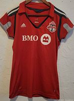Front of red Adidas Toronto FC women’s soccer top with collar, team crest, and sponsor logo