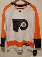 Front full view of white Philadelphia Flyers youth jersey with orange and black trim, showing logo and tags