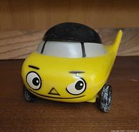 Front view of yellow plastic Mr Beep advertising car bottle opener, showing facial design with eyes and nose, black convertible roof, wear on wheels