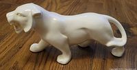Side view of a glossy white ceramic panther figurine on a wooden surface, showing the panther in a walking pose with open mouth and curled tail.