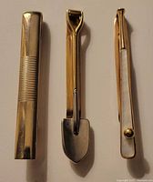 Three unique metal tie clips shown side by side on a light surface.